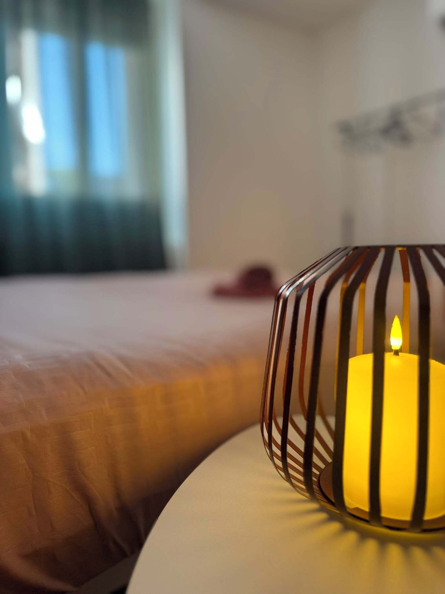 A candle in a metal holder on a bed with a white headboard.