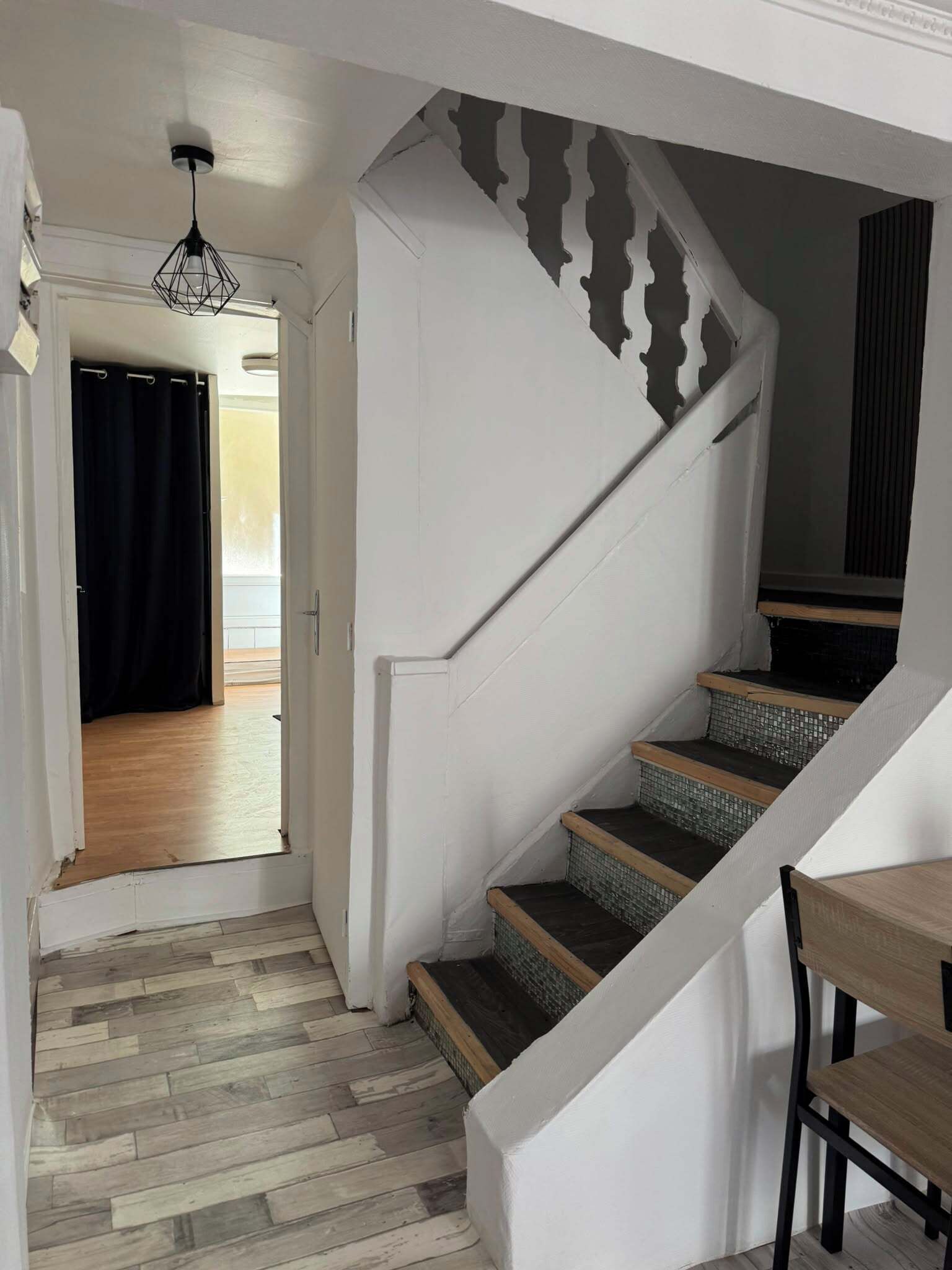 Una escalera con pared blanca y barandilla negra, que conduce a una habitación con suelo de madera.