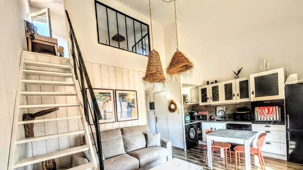 Ein modernes Interieur mit Treppe, einer Couch, einem Couchtisch, einer Küchenzeile und Pendelleuchten.