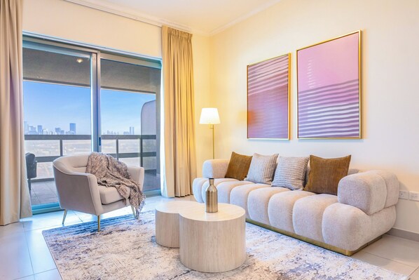 Una sala moderna con un sofá, una mesa de centro, una silla y vistas de un paisaje urbano a través de amplios ventanales.