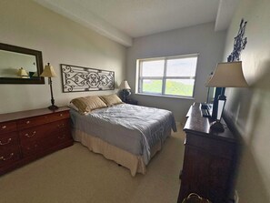 Ein Schlafzimmer mit Bett, Schminktisch, Nachttisch, Lampe, Fenster und Wanddekoration.