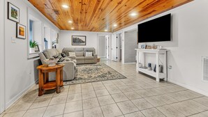 Un salon moderne avec un plafond en bois, un canapé gris, une table basse et un téléviseur fixé au mur.
