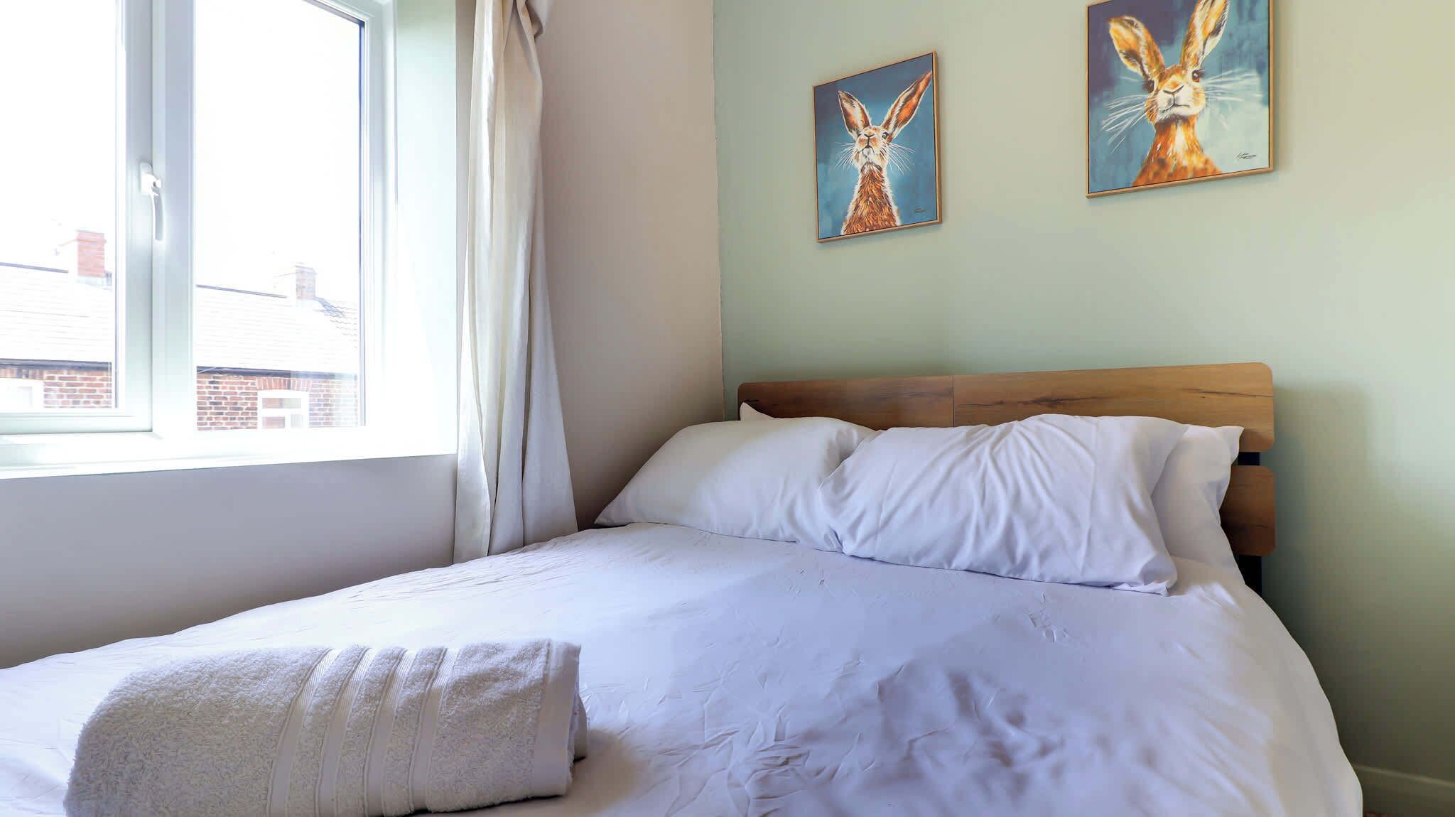 Une chambre à coucher avec un lit, une fenêtre avec des rideaux et deux tableaux accrochés au mur.