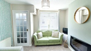 A room with a green sofa, a fireplace, a television, and a window with a view of buildings.