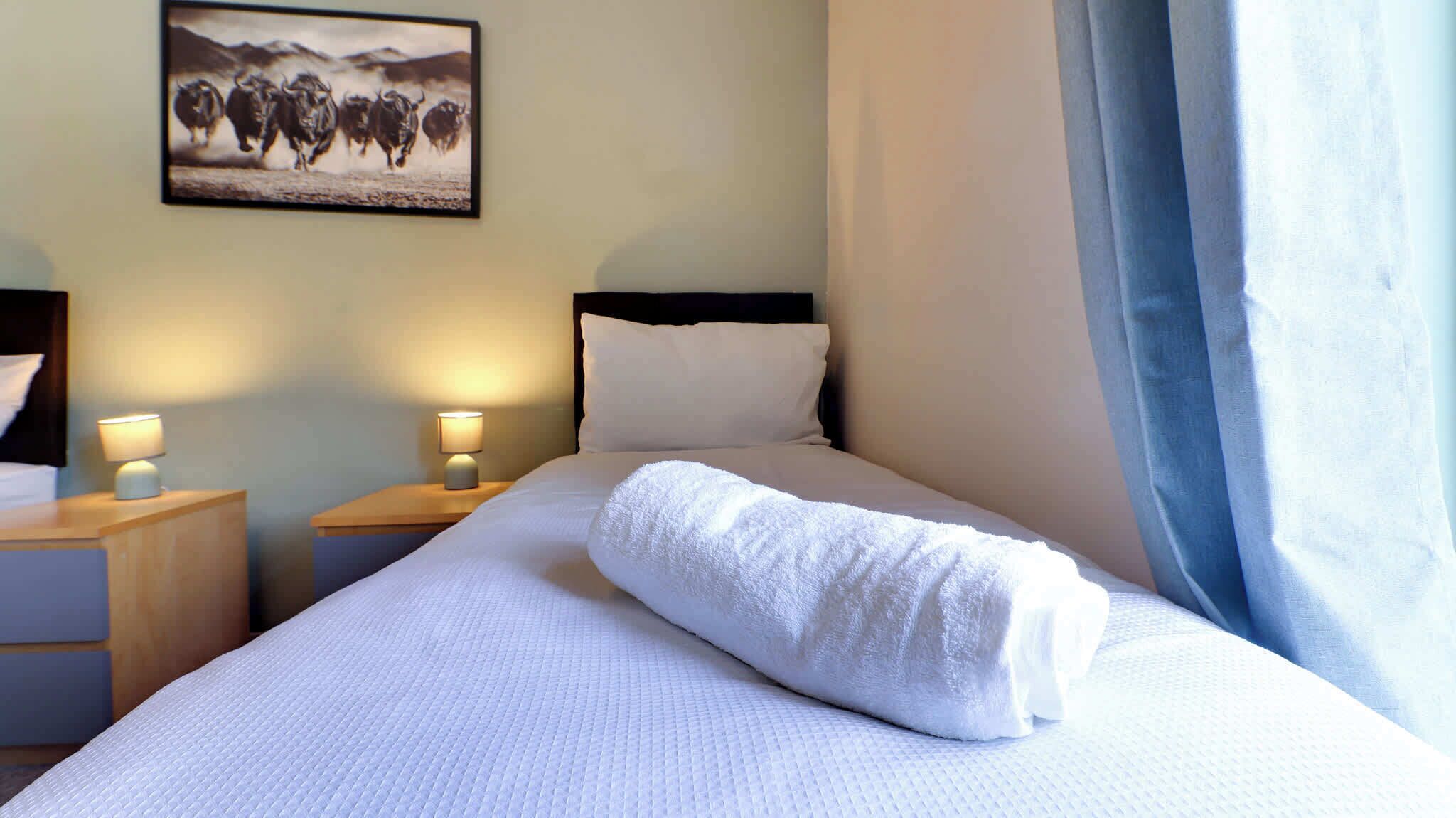 A hotel room with a neatly made bed, two bedside lamps, a headboard, and a framed picture on the wall.
