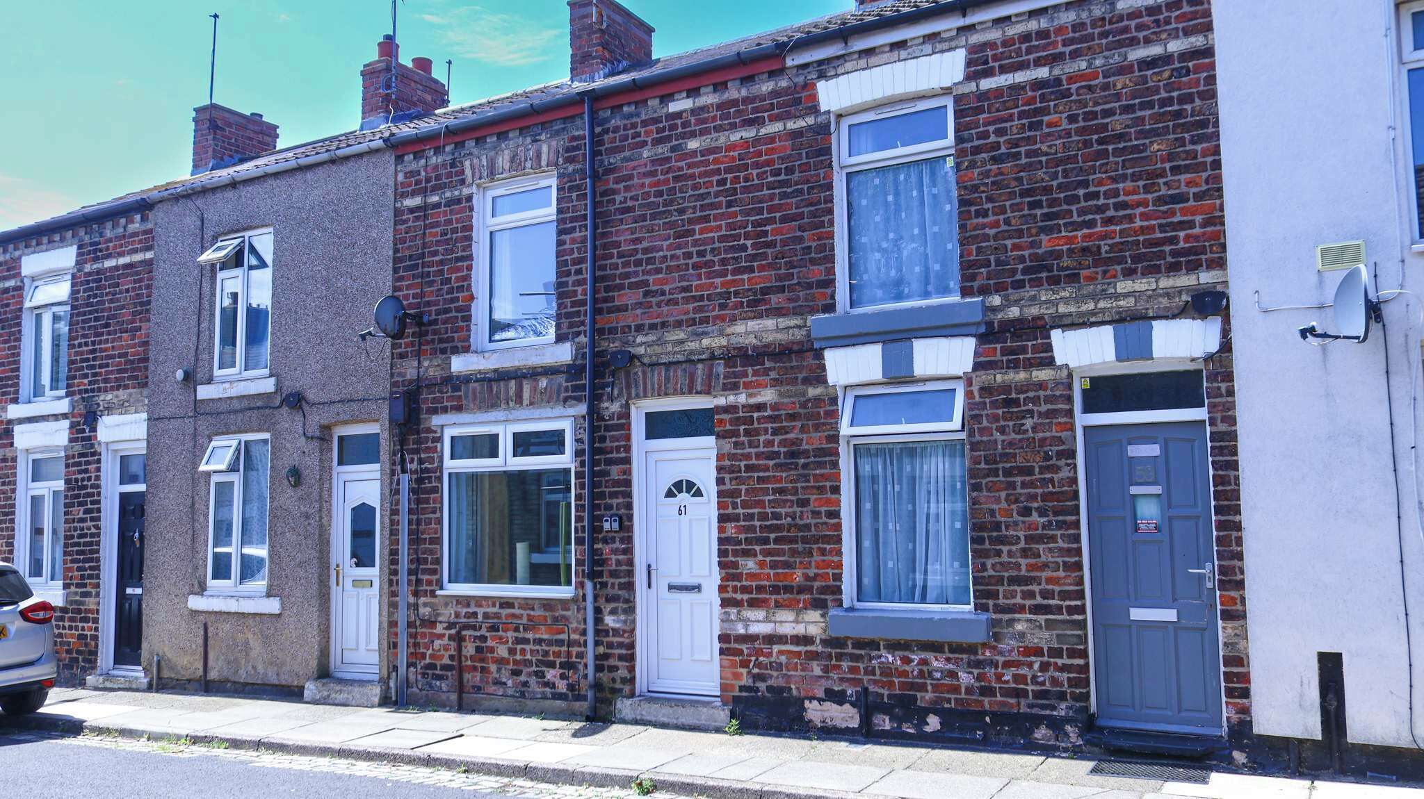 A row of terraced houses with brick facades, white doors, and windows with blue frames.