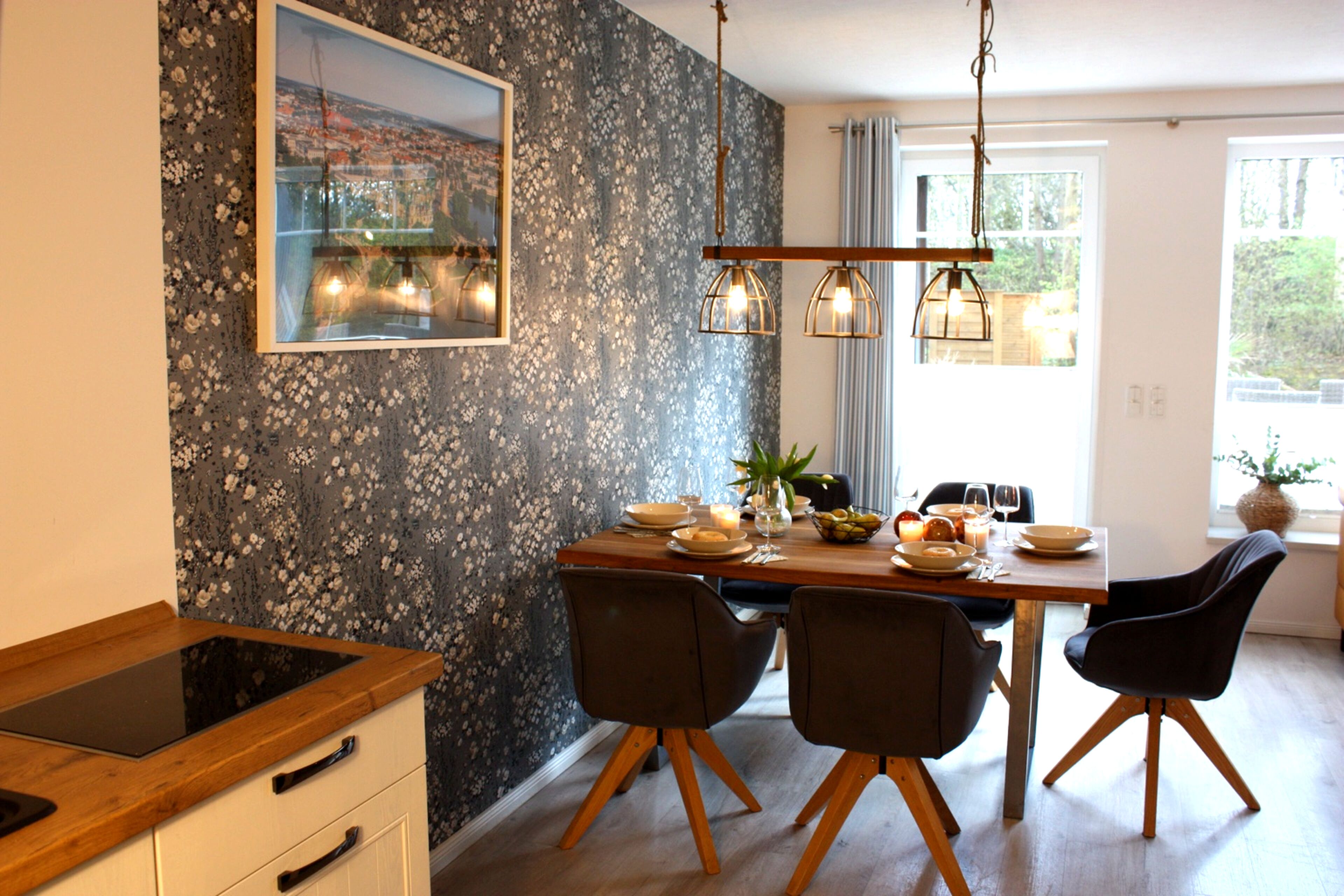 Een eetruimte met een houten tafel, vier stoelen, een vaas met bloemen en een schilderij aan de muur.