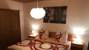 A bedroom with a bed, two bedside tables, a wooden wardrobe, a hanging light fixture, and a painting on the wall.