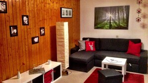 Habitació amb paret de fusta, un sofà modular negre, taula de cafè blanca i una alfàbbra vermella.