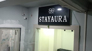 A sign for 'STAYAURA' with a logo and text, a door with a glass panel, and a red electrical box. - STAYAURA BY ROH (Guwahati)
