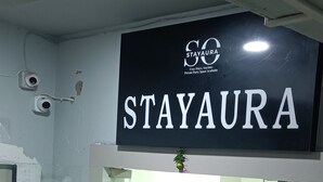 A sign for StayAura, a private party space, with a glass partition and a black sofa. - STAYAURA BY ROH (Guwahati)