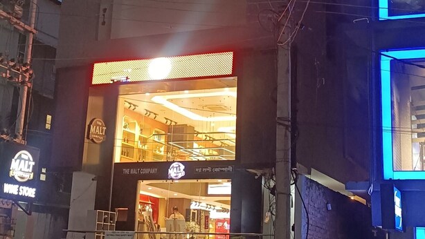 A building with a sign for 'Chain of Clouds' and 'Stayura' on the ground floor, a wine store on the left, and a brightly lit entrance. - STAYAURA BY ROH (Guwahati)