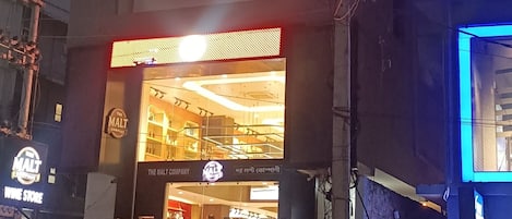 A building with a sign for 'Chain of Clouds' and 'Stayura' on the ground floor, a wine store on the left, and a brightly lit entrance.