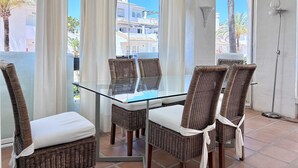 Un balcon avec des fauteuils en osier, une table en verre et une vue sur les immeubles et les palmiers.