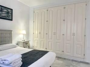 A neatly made bed with white linens and a grey throw, a bedside lamp, and a large white wardrobe with multiple doors. - Fantastic 2 Bedroom Duplex Pool View Fase 6 (Marbella)