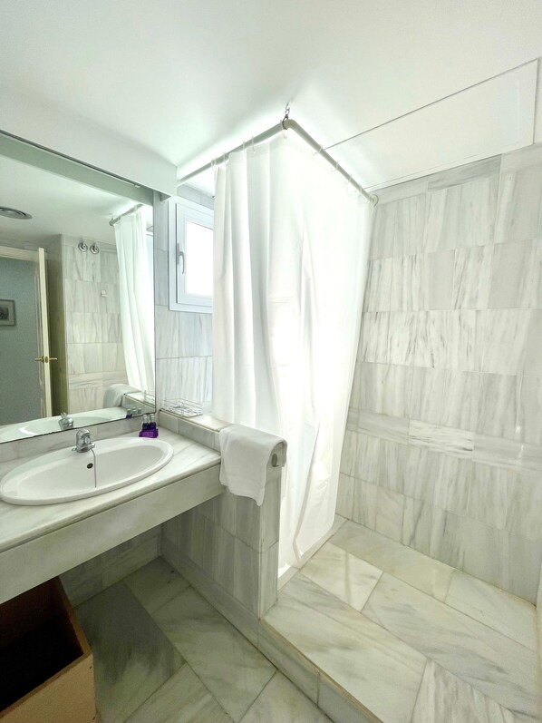 Un baño con lavamanos, espejo, cortina de ducha y paredes de azulejos.