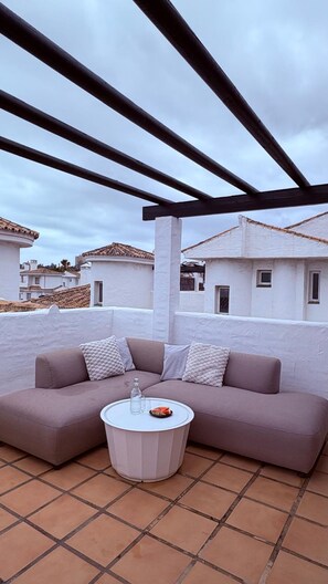 A patio with a sofa and a round table, white walls, and a tiled roof. - Modern Duplex 3 Bedroom F72 (Marbella)