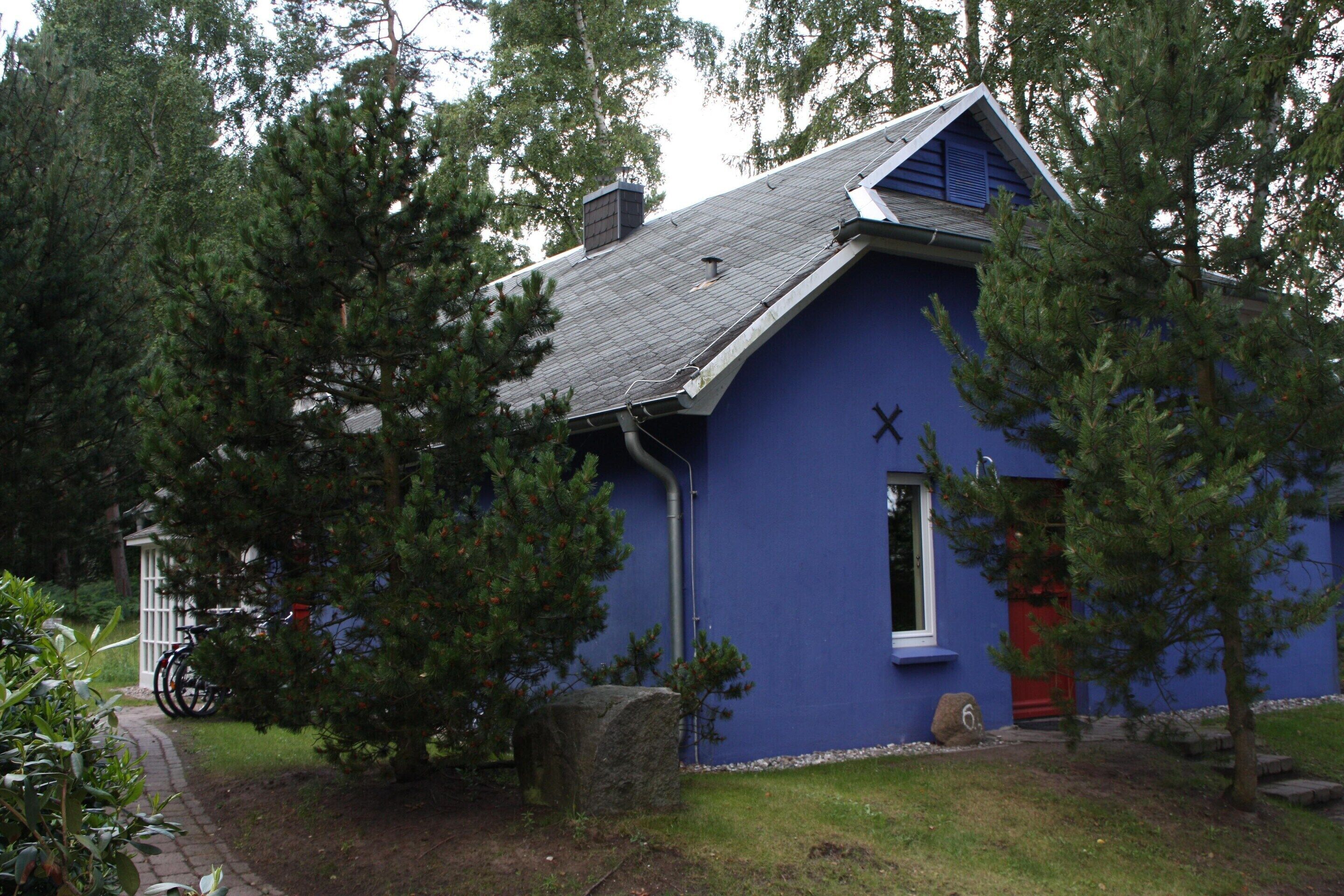 A blue building with a sloped roof, a red door, and a window with a cross symbol.