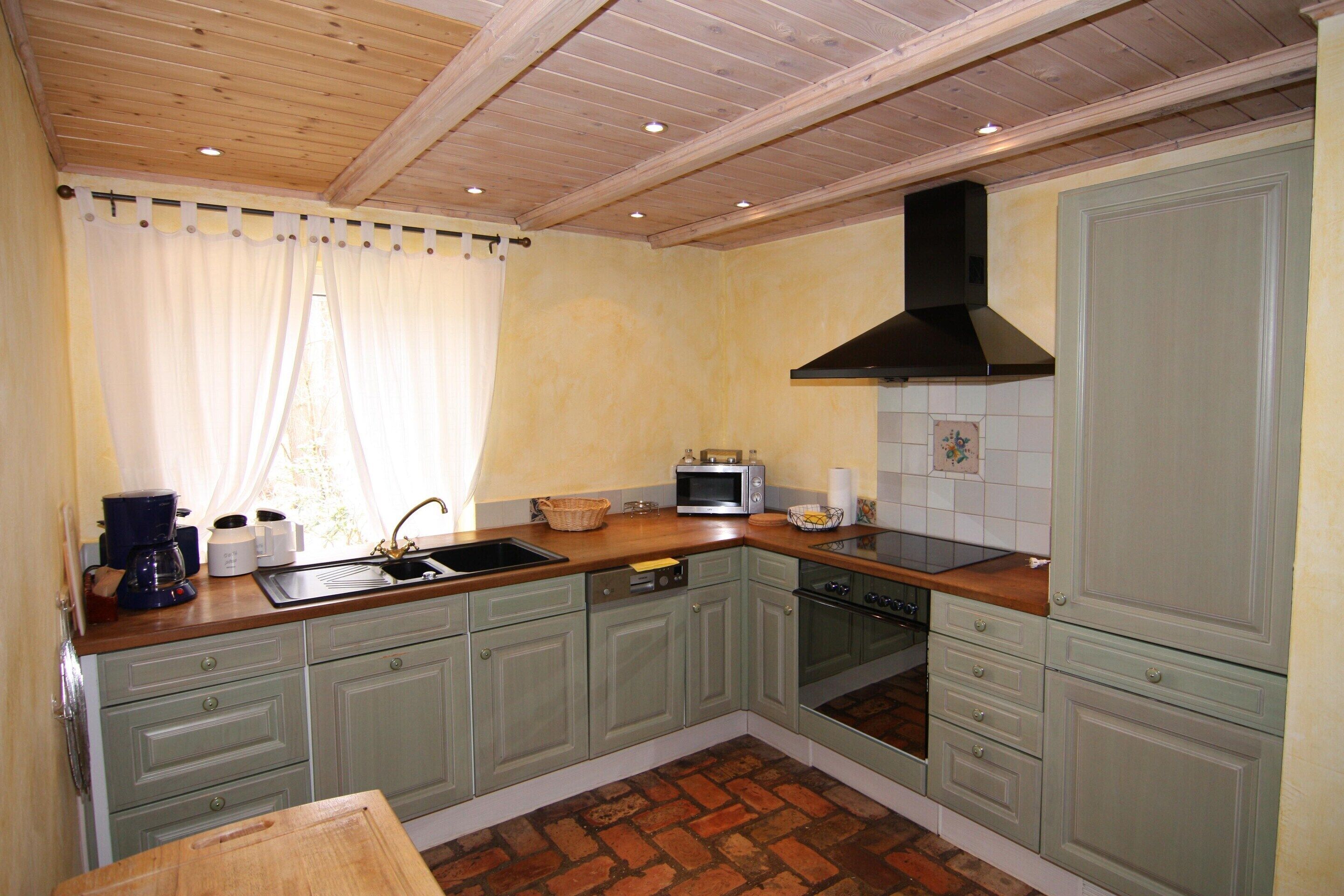 A kitchen with green cabinets, a black range hood, a microwave, and a sink.