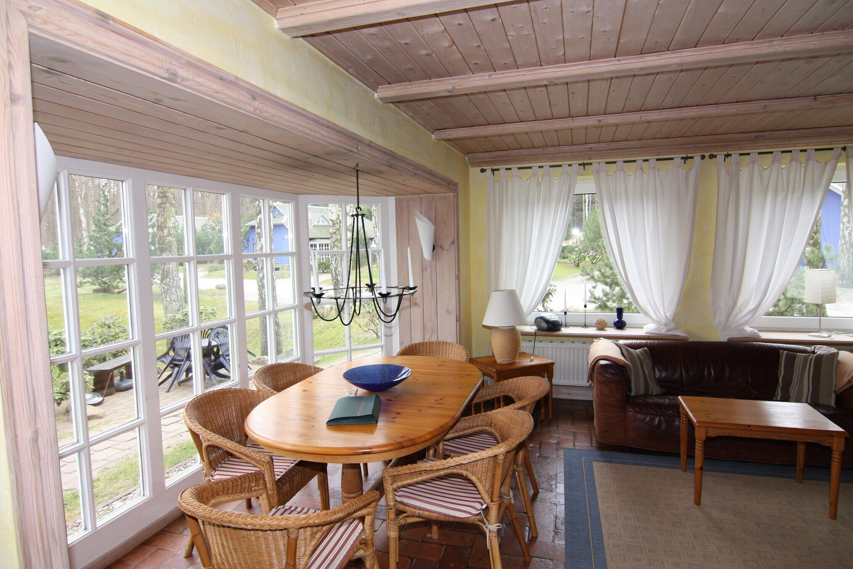 A room with a dining table, wicker chairs, a sofa, and a window with curtains.