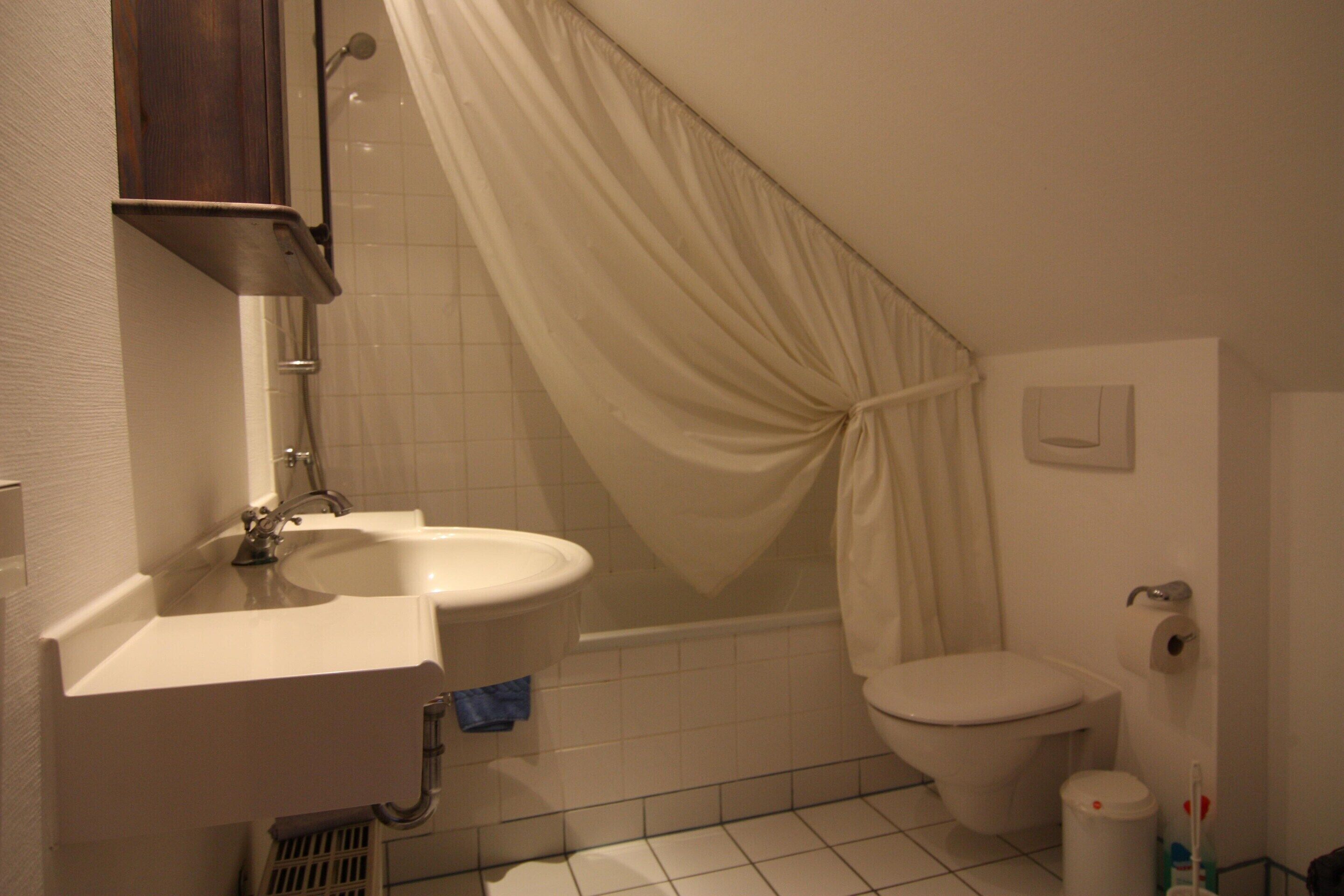 Une salle de bain équipée d’un lavabo, de toilettes, d’un rideau de douche et d’une petite poubelle.