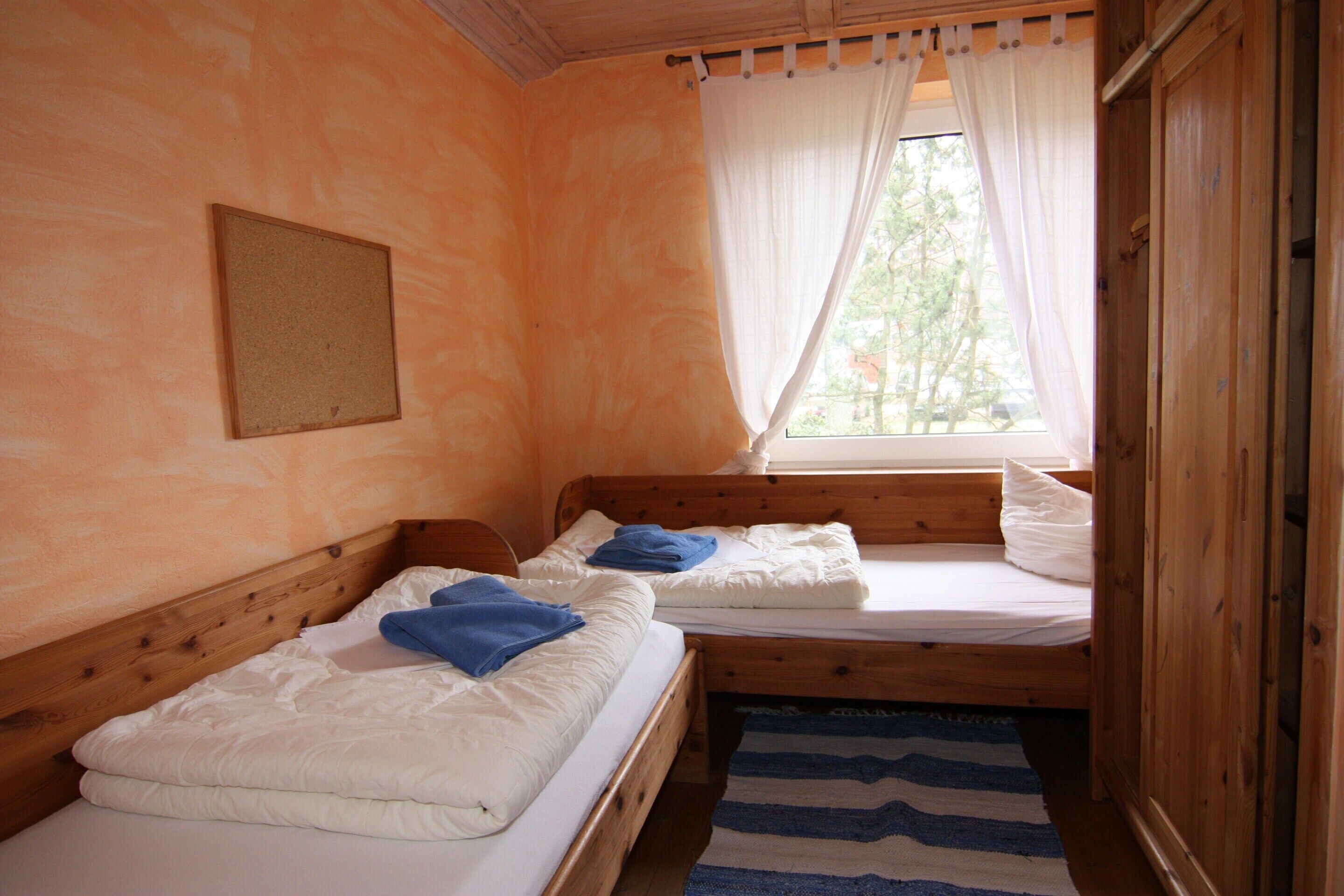 Una habitación con dos camas de madera, una ventana con cortinas, un armario de madera y un tapete azul a rayas.