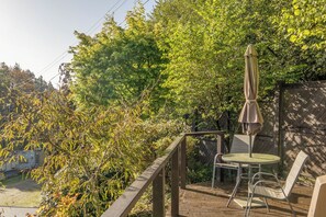 Eine Holzterrasse mit Tisch und Stühlen, umgeben von dichter Vegetation und einem Holzzaun.