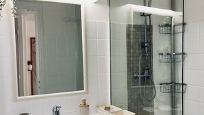 Une salle de bain moderne avec une douche à parois de verre, un meuble-lavabo blanc avec un miroir et une petite plante en pot.