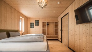 A wooden-paneled bedroom with a bed, built-in shelves, a TV, and a chandelier. - Chalet With Mountain Views, Dein Bichlbach (Bichlbach)