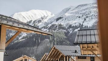 A mountain cabin with large windows, wooden beams, and a view of snow-covered mountains.