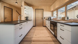 A modern kitchen with wooden walls, a central island, and a view of the mountains. - Chalet With Mountain Views, Dein Bichlbach (Bichlbach)