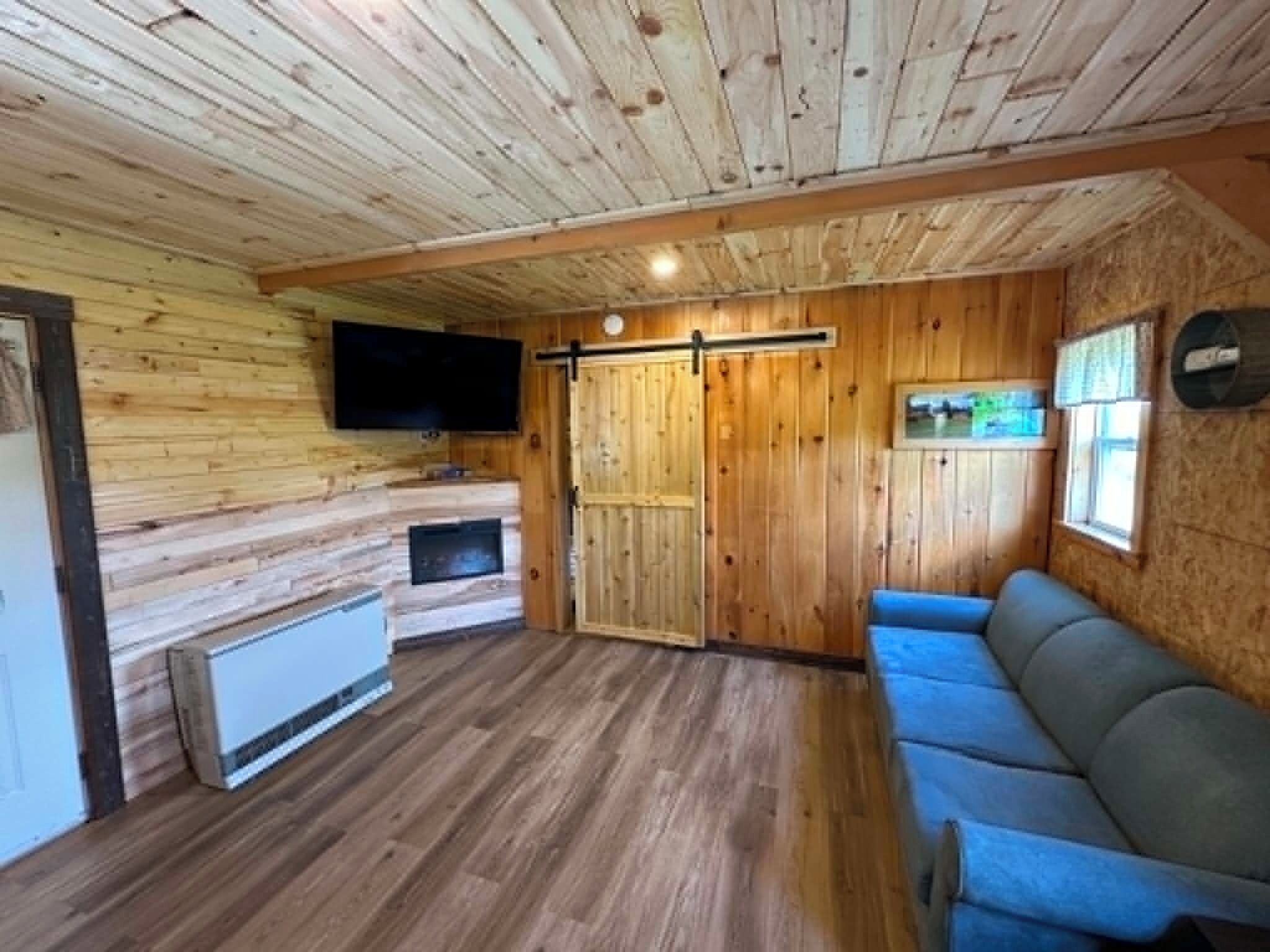 Ein Holzinnenraum mit Fernseher, einer Schiebetür, einer Couch und einem Kamin.