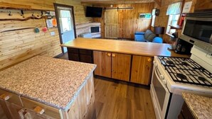A wooden cabin interior with a kitchen area, a dining table, and a seating area.