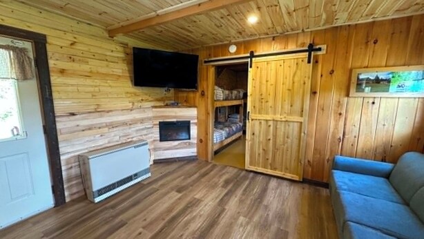 A wooden cabin interior with a television, a sliding door, a sofa, and a fireplace.