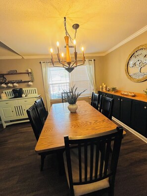 A dining area with a wooden table, black chairs, a chandelier, and a window with blinds. -  3-bedroom house with above ground pool  in a quiet neighborhood in Little River (Little River)