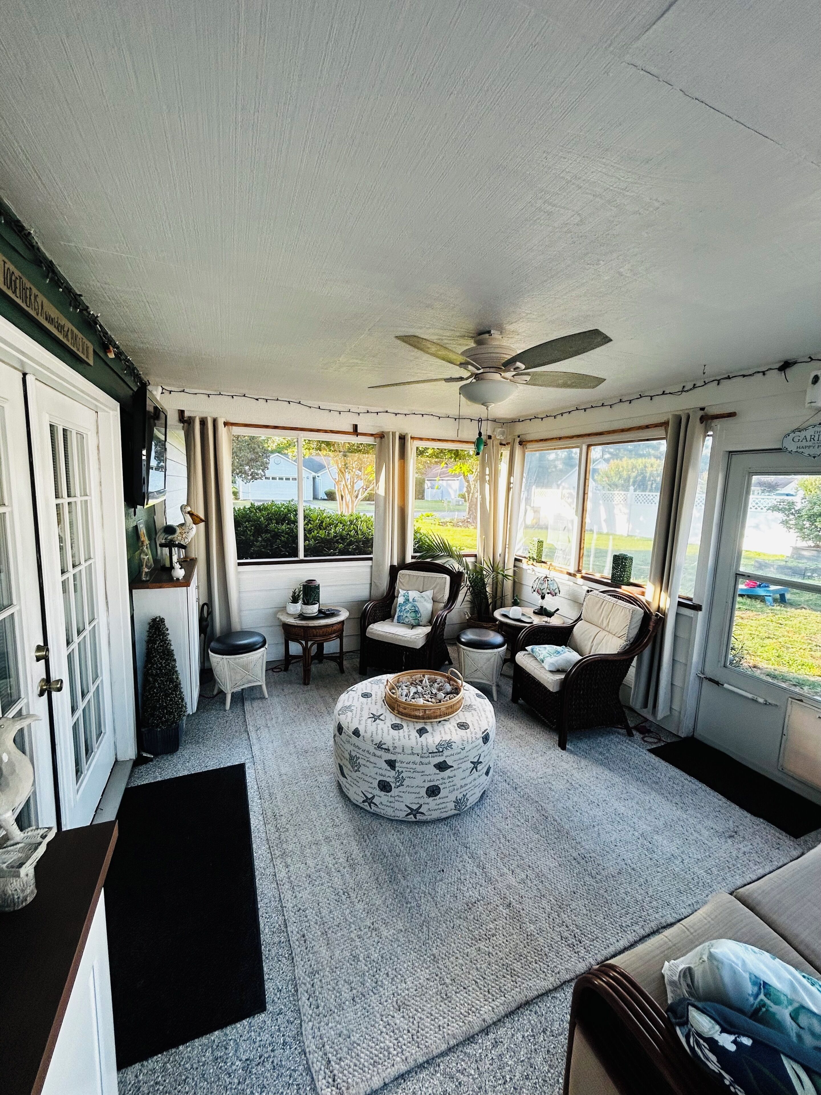 A sunlit room with a ceiling fan, a round ottoman with a starfish pattern, and a dining table with chairs.