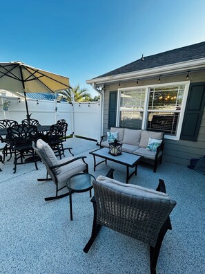 An outdoor patio area with a dining table, chairs, a sofa, and a small round table. -  3-bedroom house with above ground pool  in a quiet neighborhood in Little River (Little River)