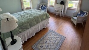 A bedroom with a bed, a desk, two chairs, a lamp, and a rug.