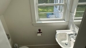 A small, white bathroom with a window, a toilet, a sink, and a shower.