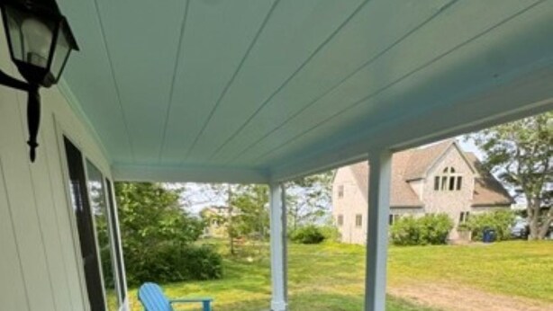 A covered porch with a wooden deck, a lamp post, and blue Adirondack chairs.