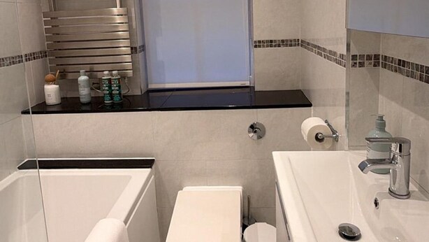 A modern bathroom with a bathtub, toilet, sink, and a window with a blind. - West End Elegance - by Out of Office Lifestyle (London)