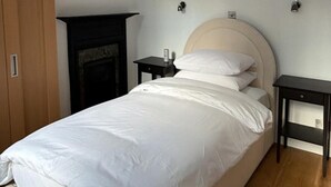 A bedroom with a bed, a wooden wardrobe, a fireplace, and two bedside tables. - West End Elegance - by Out of Office Lifestyle (London)