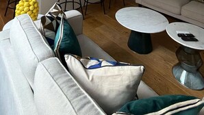 A modern living room with a sofa, a coffee table, and a dining area with chairs and a kitchen in the background. - West End Elegance - by Out of Office Lifestyle (London)