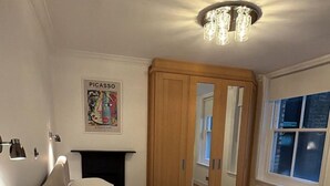 A bedroom with a bed, a round table with a can, a mirror, a fireplace, and a window. - West End Elegance - by Out of Office Lifestyle (London)
