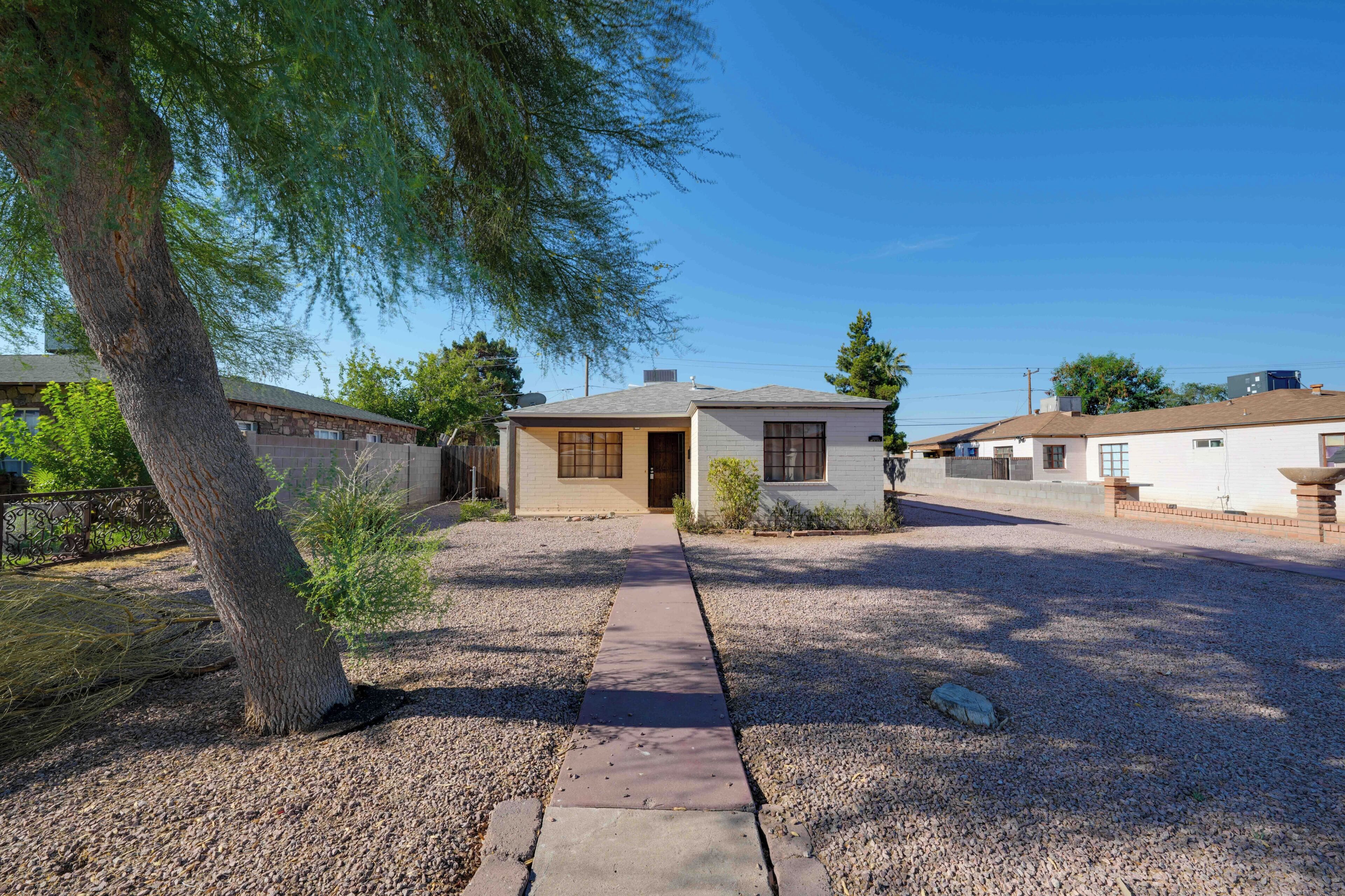 A residential area with a house featuring a front yard, a gravel driveway, and a large tree.