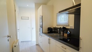 A modern kitchen with a black countertop, white cabinets, and a window with blinds. - Holiday Home in Otterlo With Terrace (Otterlo)
