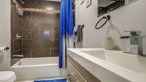 Et badeværelse med badekar, bruser, vask og toilet.