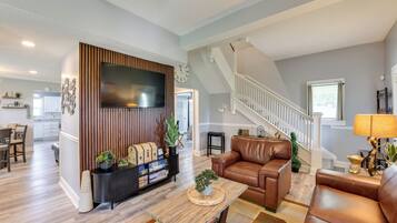 Amplia sala de estar con una chimenea moderna, sofás de cuero, un televisor de pantalla plana y una escalera que conduce a un nivel superior.