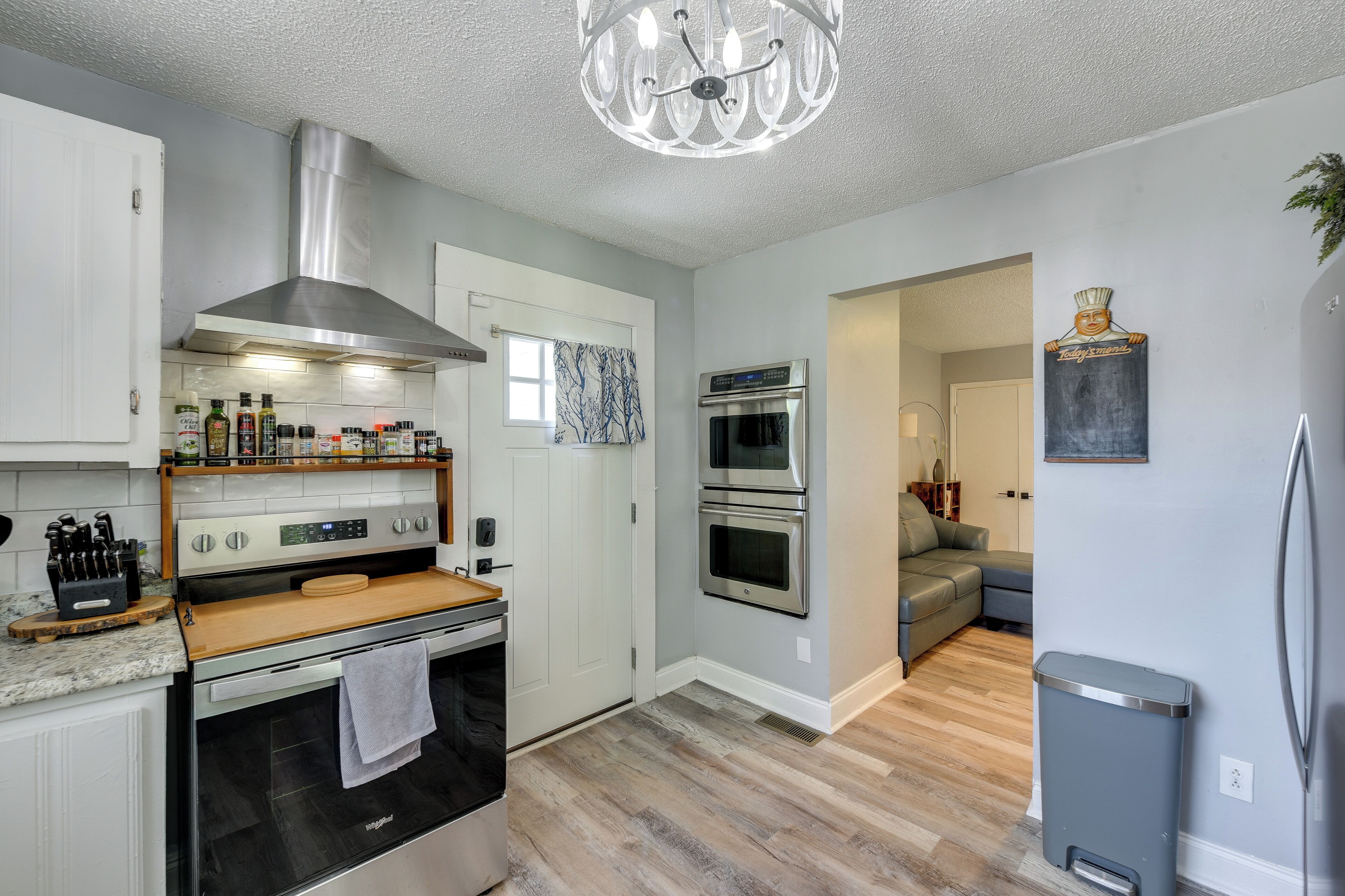 A modern kitchen with stainless steel appliances, a wooden countertop, and a chandelier.