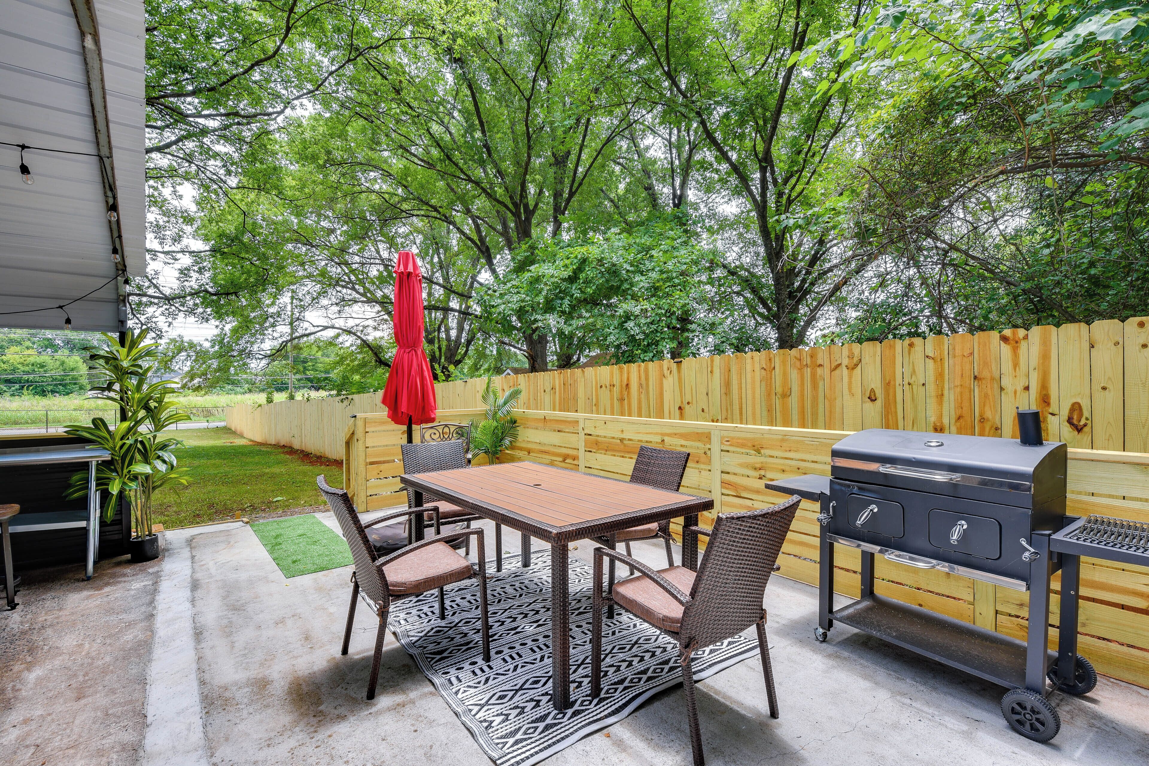 An outdoor patio with a grill, dining table, chairs, and a red umbrella.
